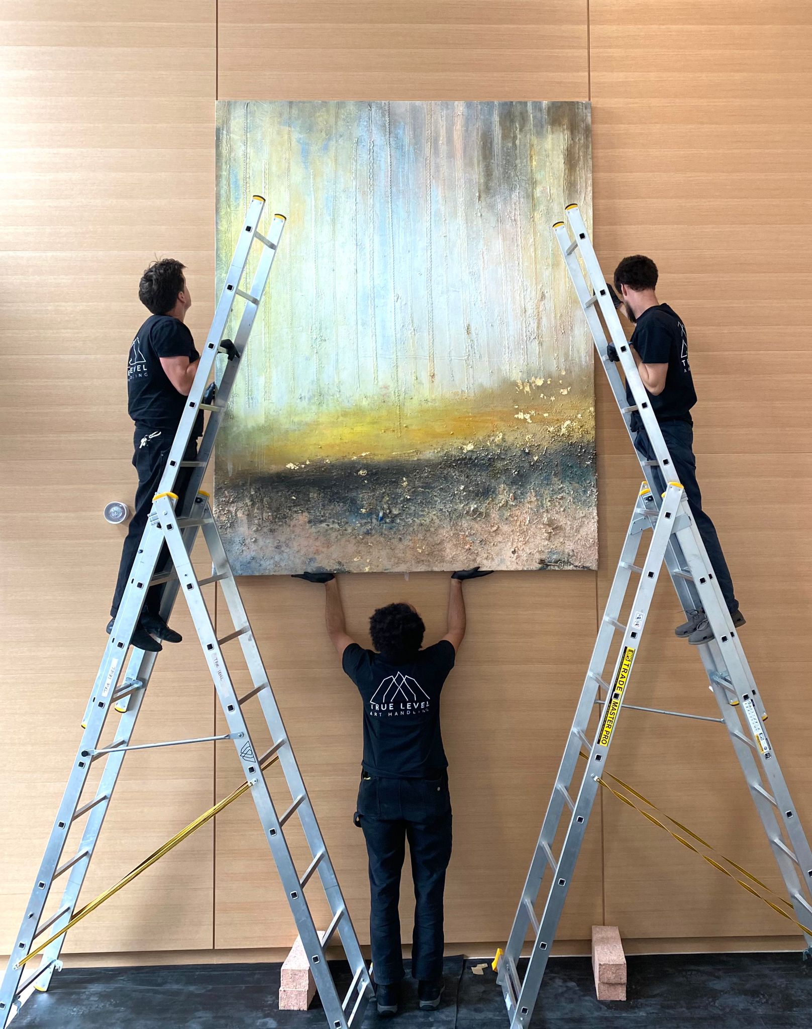 Three True Level Art Handling experts hanging a large piece of art safely on ladders.