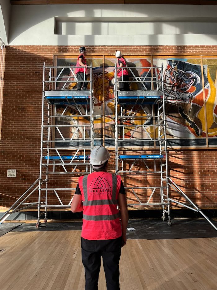 A large piece of artwork being installed by three True Level technicians