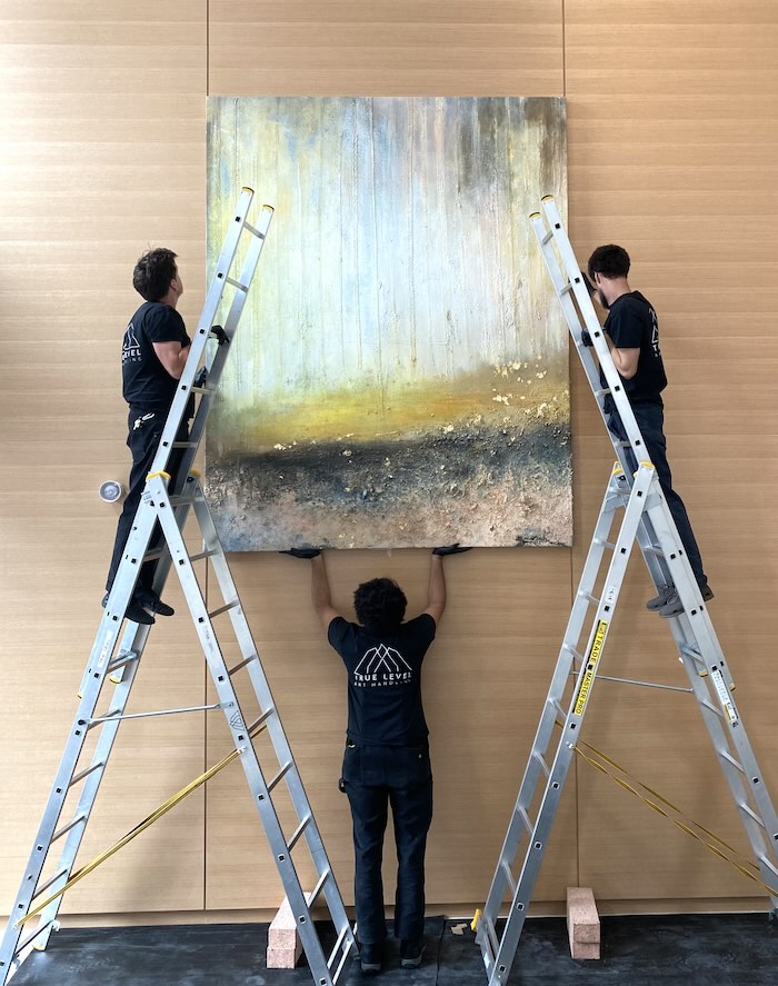 A large piece of artwork being installed by three True Level technicians